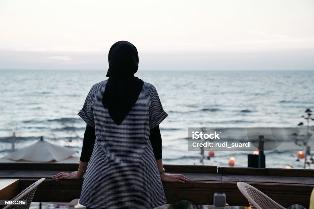 muslim woman looking the beach from the deck One Woman Only Stock Photo