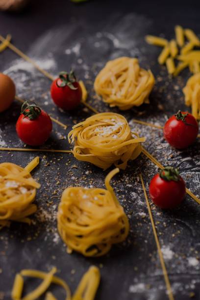 istock Vertical closeup of raw pasta prepared in a nicely decorated setting with tomatoes, black background 1455023163