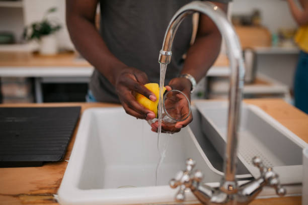 Close-up of young man washing a glass in sink at home stock photo