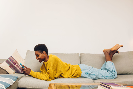 African woman using cellphone at home sitting on the sofa