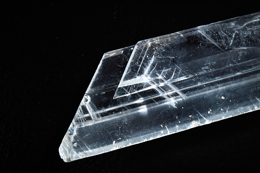 A closeup of a rare mineral row uncut transparent crystal on a black background