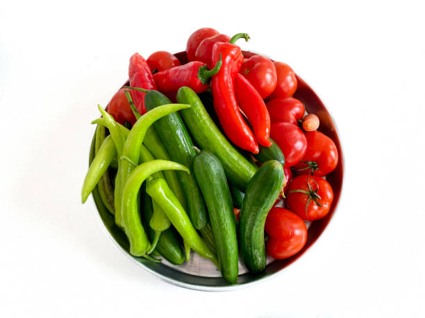 Fresh cucumbers, tomatoes, green peppers and red peppers in the metal strainer on Isolated white background
