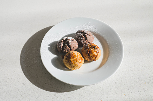 Top view of chocolate and walnut ball cookies served on a white plate under harsh sunlight