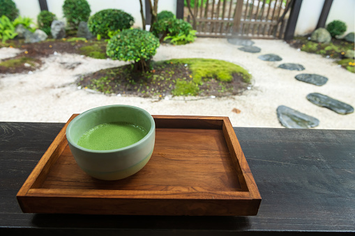 Hot macha green tea on wooden table with traditional Japanese garden. Japan famous drink in spring park.