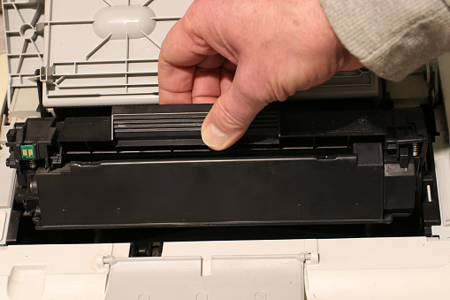 A man changes a toner cartridge in a laser printer.
