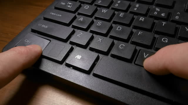 A black keyboard of a computer and a man's hands pressing the CTRL and C keys to do the copy, and then CTRL and V keys to do the paste command. Close up shot
