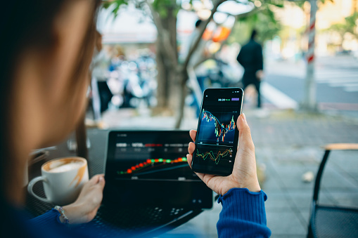 Mujer de negocios mano usando teléfono inteligente con cafetería. Gráficos del mercado de valores en la pantalla del teléfono y la computadora portátil. Comprobación del mercado financiero. photo