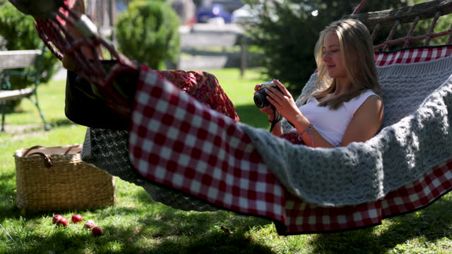 Teenage girl resting on hammock and reviewing photos on a retro mirrorless camera