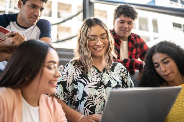 giovane donna che mostra qualcosa sul computer portatile ai suoi amici sulle scale dell'università - university student laptop campus foto e immagini stock