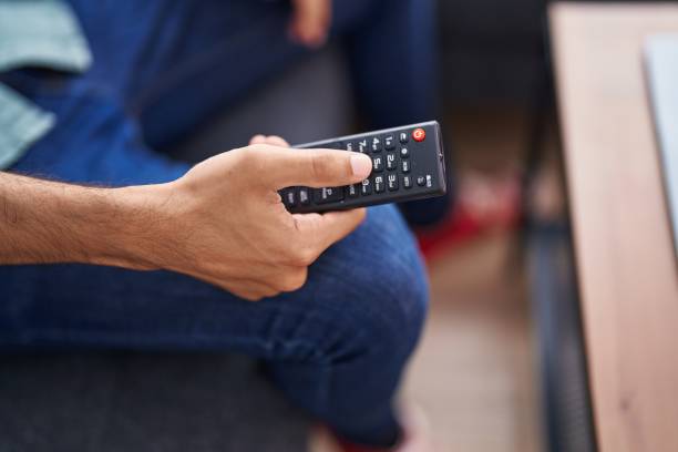 istock Young hispanic man holding tv remote control sitting on sofa at home 1455042184