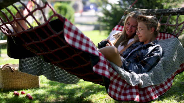 Teenage kids resting on hammock and reviewing photos on a retro mirrorless camera