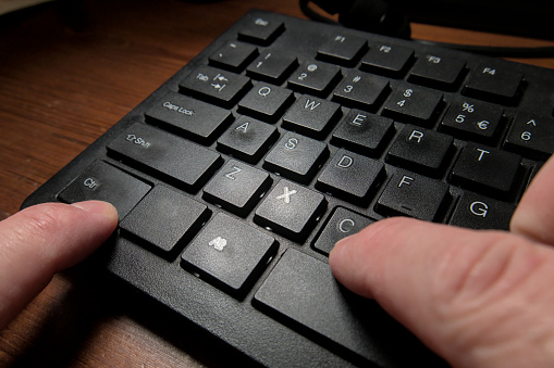 A black keyboard of a computer and a person's hands pressing the CTRL and C keys to do the copy command. Close up shot