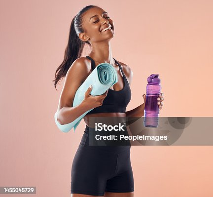 istock Happy, fitness and healthy while holding exercise mat and water bottle against peach studio background. Fit woman with slim body after exercise, training and sports workout and vitality healthcare 1455045729
