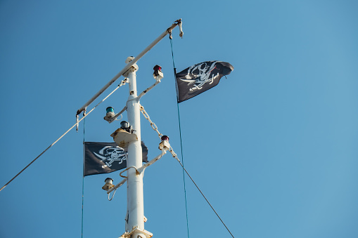 Jolly Roger or pirate ship flag waving with flagpole and blue sky, skull and crossbones, Pirates of the Caribbean sea and Black Pearl. Ripped tear
