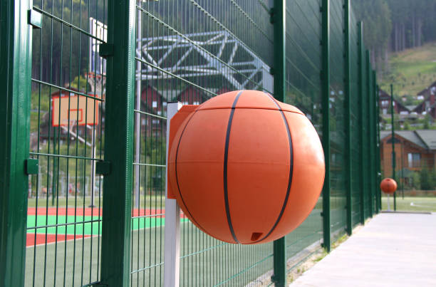 botes de basura de plástico en forma de pelota de baloncesto en la acera de concreto alrededor de la cancha de baloncesto - wastepaper basket fotografías e imágenes de stock