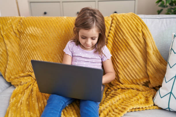 istock Adorable hispanic girl using laptop sitting on sofa at home 1455047406