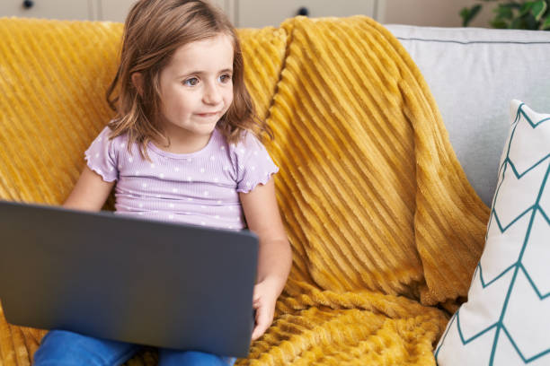 istock Adorable hispanic girl using laptop sitting on sofa at home 1455047413