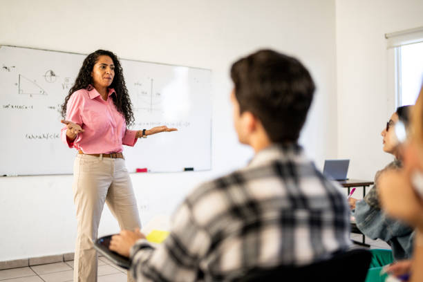 istock Mid adult teacher explaining lesson to university students in the classroom at university 1455047480