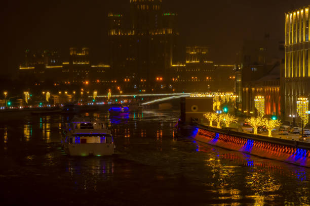 City embankment decorated with gold colored illuminated tree shaped artificial Christmas decorations at night. Tourboat on water. Selective focus. Winter holidays theme.