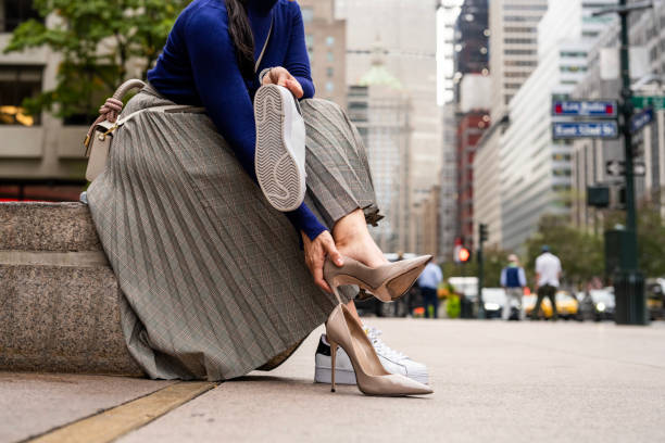Close up on businesswoman’s feet while she is changing high heels into sneakers in the street in front of a building where she is working after finishing work and heading home.