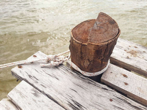 węzeł żeglarski zawiązany na drewnianym słupku. słupek na drewnianych deskach w mętnych wodach mekongu. zbliżenie starego drewnianego stanowiska cumowniczego. - moored nautical vessel tied knot sailboat zdjęcia i obrazy z banku zdjęć