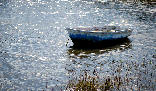 A small blue rowing boat sits on a sparkling sunlit sea conveying a sense of calm and tranquility.