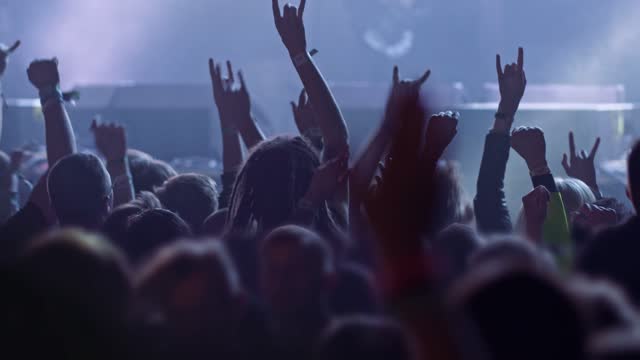 Fans at rock concert. People raising and claping their hands in stage lights. Unrecognizable fans dancing at a concert or festival party. Silhouettes of concert crowd in front of bright stage lights, Concert fans