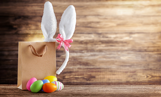 in the shopping bag there are Easter bunny ears and multicolored eggs, on a wooden background with a place for text