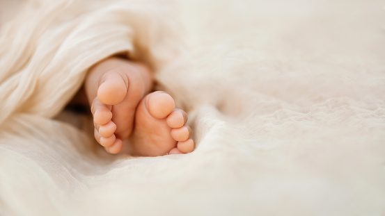 Newborn baby feet closeup on soft cream wrap in a selective focus