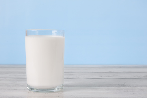 The glass full of milk on wooden table. Glass of fresh white milk on blue background in the kitchen.