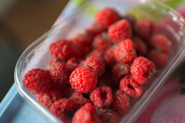 Close up of a plastic recipient with raspberries in bad condition. Bright red color