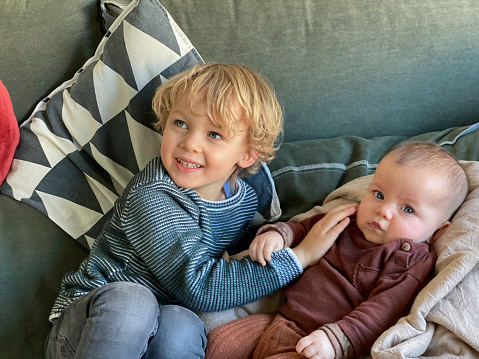 Toddle boy playing with his baby sister on the sofa