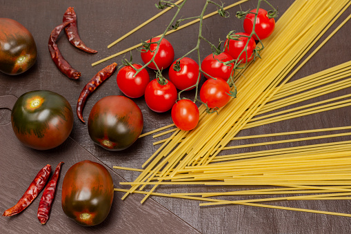 Spaghetti, cherry tomato sprig and whole brown tomatoes. Top view. Brown background.
