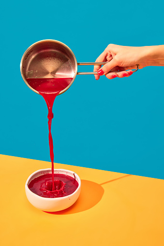 Woman pouring traditional Ukrainian dish, borscht into plate on yellow tablecloth over blue background. Red Beet soup. Popular dinner. Food pop art photography. Complementary colors. Copy space for ad