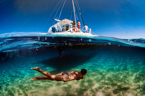 split shot, above underwater woman swimming from a sailboat catamaran in cozumel, mexican caribbean