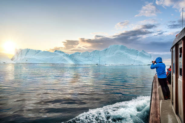 Travel in arctic landscape nature with icebergs, tourist man explorer from a boat at sunset. Greenland Tourists in a boat in front of an iceberg taking photos at midnight sun sunset, Ilulissat Icefjord, Disko bay, Greenland disko bay stock pictures, royalty-free photos & images