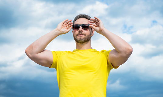 face of man in yellow shirt and sunglasses outdoor on sky background.