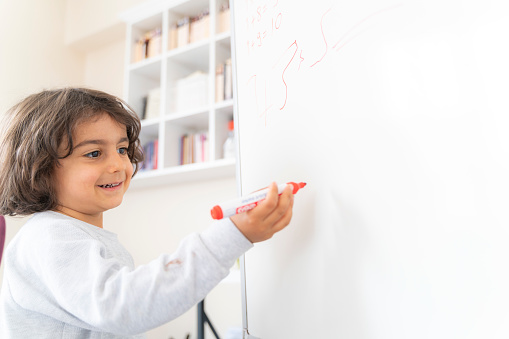 little boy writing on blackboard with red pen. There is a library at the back. Shot with a full-frame camera in daylight.