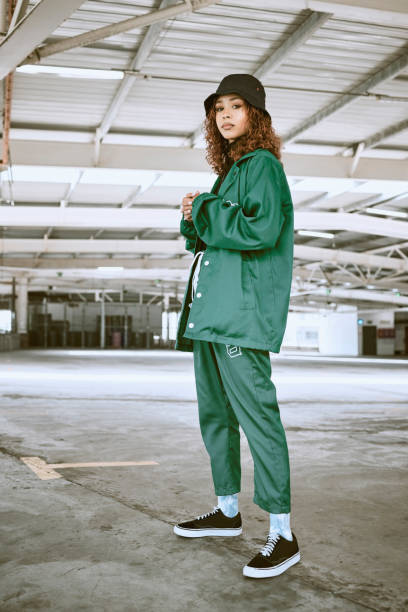 portrait, fashion or stylish young gen z woman stand in a warehouse with green clothing. trendy, hipster latino girl with attitude and curly hair in industrial building or factory with pride or cool - generatie z stockfoto's en -beelden