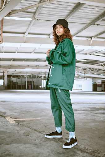 Portrait, fashion and stylish young gen z woman standing in a warehouse while wearing green clothing. Trendy, hipster latino girl with curly hair in industrial building or factory with pride or cool