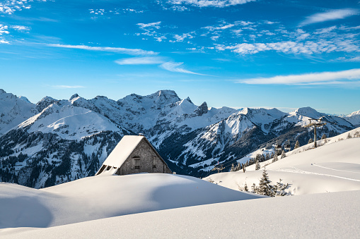 Beautiful winter scenery with trees and mountain tops in the Alps on a sunny day with blue sky and clouds.