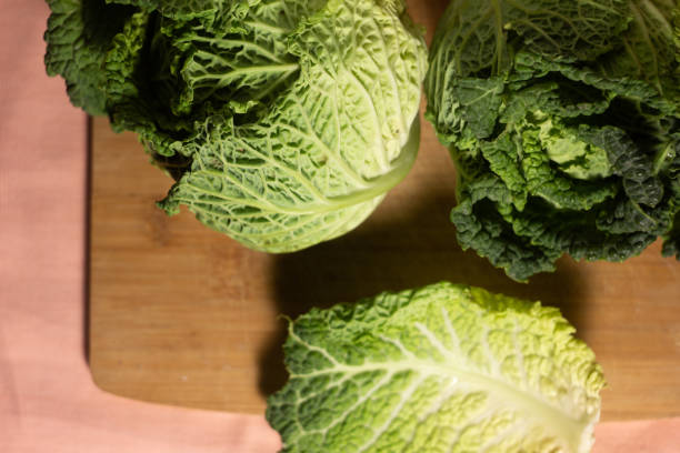 istock Top view on a wooden bamboo cutting board two savoy cabbage on a pink background with one leaf lying apart 1455099394