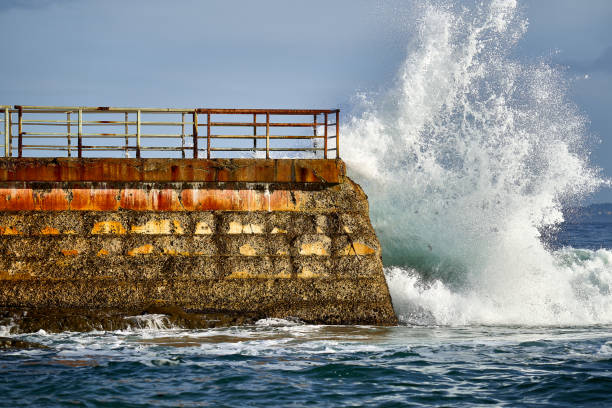 bela foto de água ondulada espirrando e colidindo em uma ponte de cais de pedra contra um céu azul - splaching - fotografias e filmes do acervo