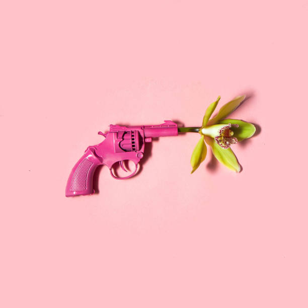 istock Flower and gun on pastel light pink background. Minimalistic love concept. Creative peace flat lay idea. 1455106960