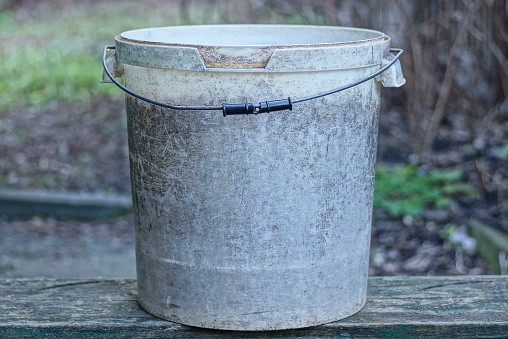 one big old dirty white gray plastic bucket stands on a table outside