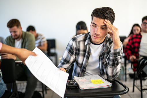 The girl sitting confusedly with her hands on her head in the school desk and attends classes. Selective focus . High quality photo