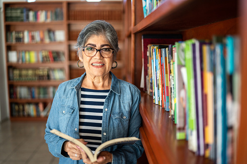 Portrait of a senior woman holding book in university library