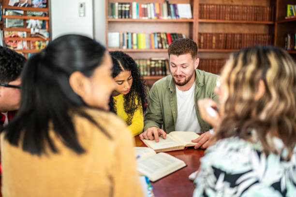 istock Young friends reading a book together in university library 1455112456