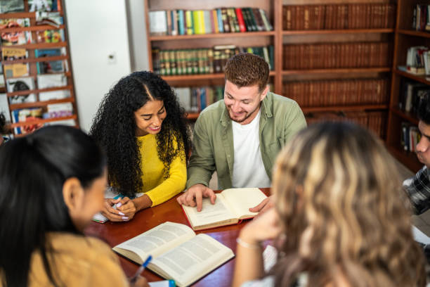 istock Young friends reading a book together in university library 1455112459