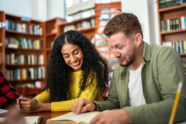 istock Young friends reading a book together in university library 1455112471